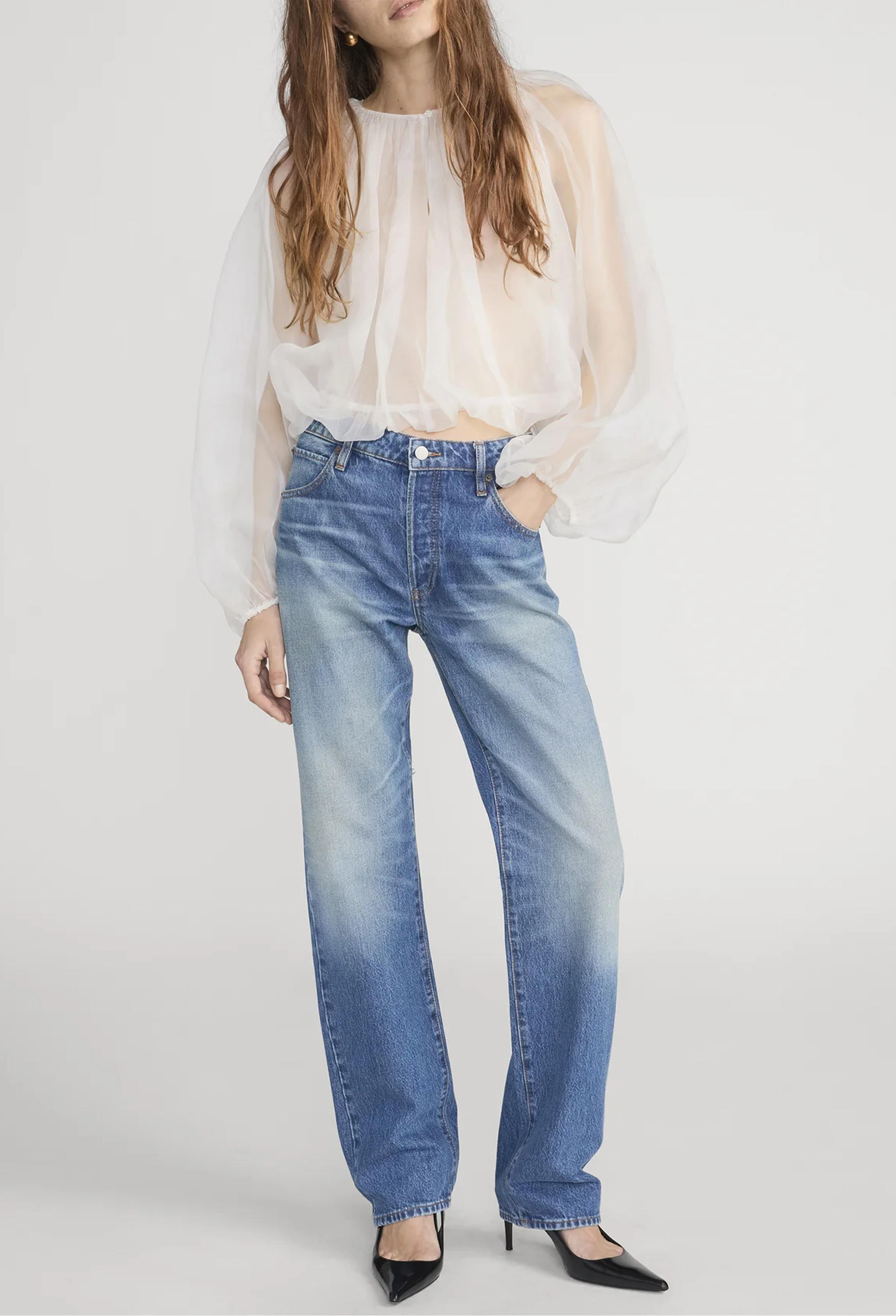 Person wearing a white blouse and blue jeans on a plain background