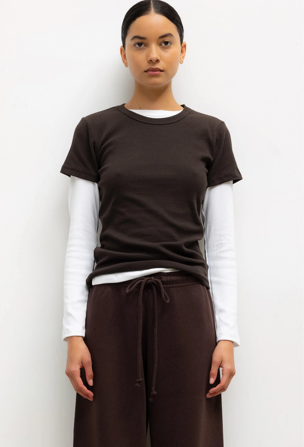 Person wearing a brown t-shirt over a white long-sleeve shirt with brown pants on a white background