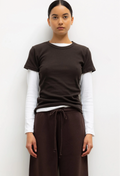 Person wearing a brown t-shirt over a white long-sleeve shirt with brown pants on a white background