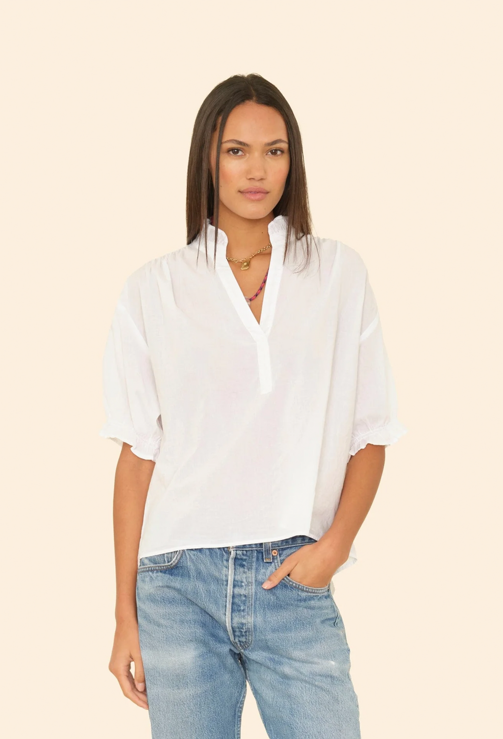 Woman wearing a white blouse and blue jeans against a beige background