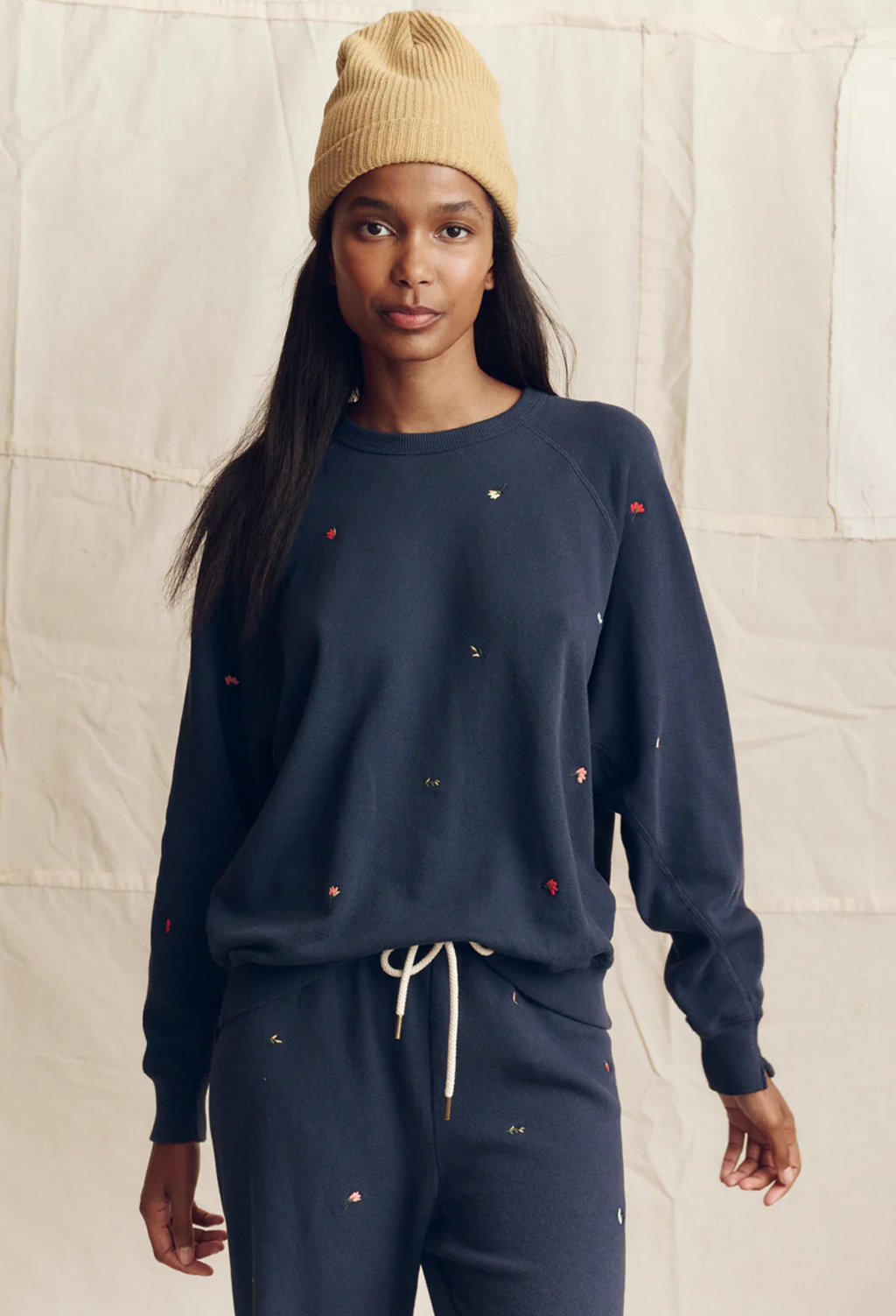 Woman wearing a navy blue sweatshirt and pants with small red and white details, standing against a plain background.