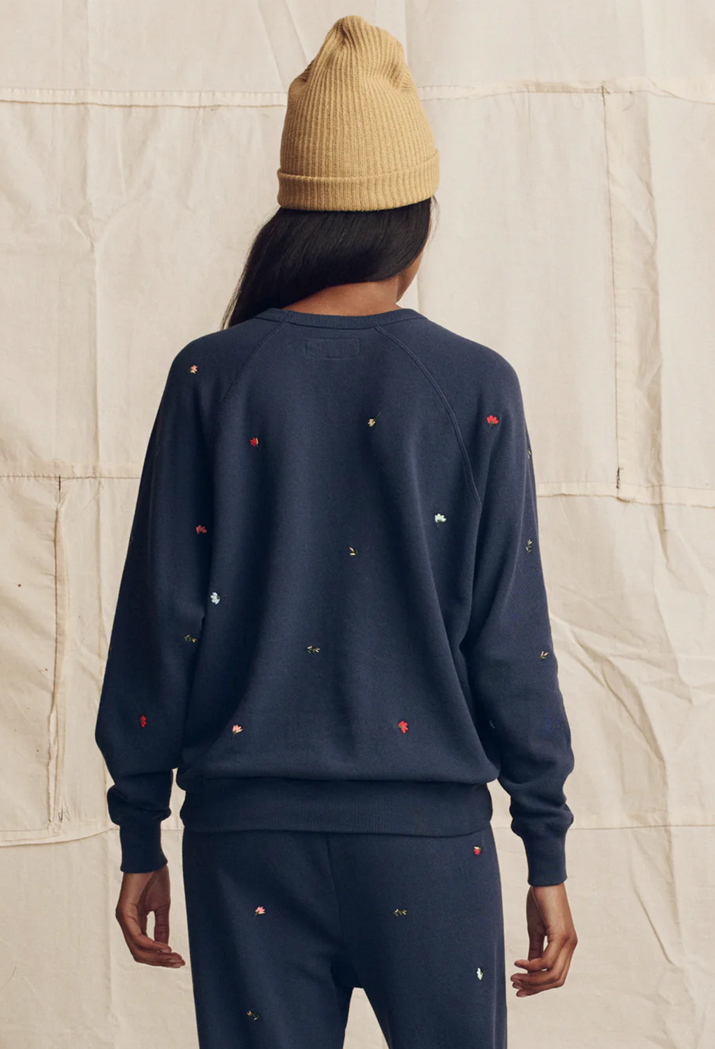 Person wearing a navy sweatshirt and pants with small red and white patterns, standing against a textured beige wall.