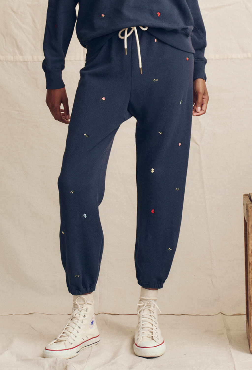 Person wearing navy jogger pants with small colorful dots and white high-top sneakers on a neutral background