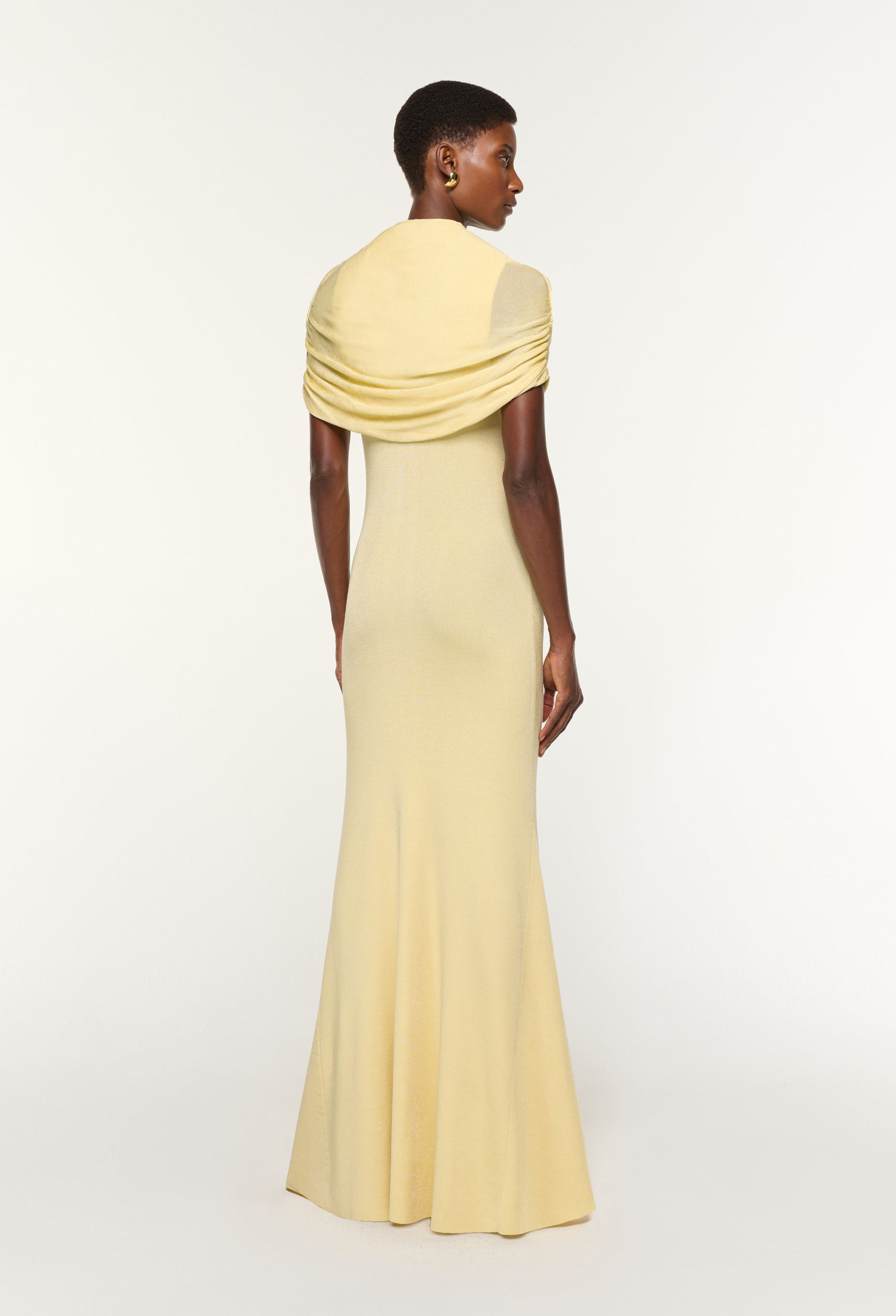 Woman wearing a light yellow evening gown with a draped effect on a white background