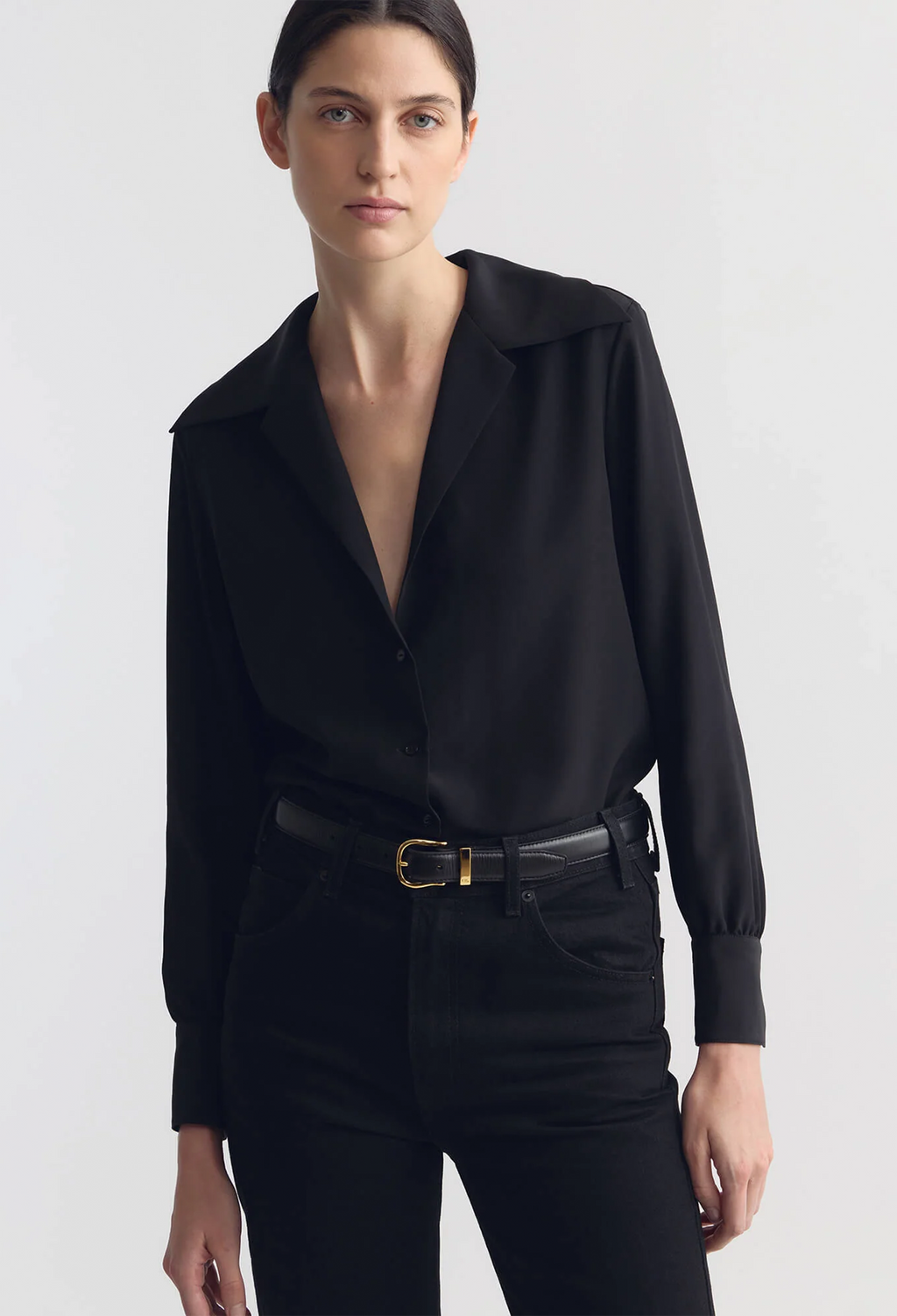 Woman wearing a black blouse and pants with a belt on a white background
