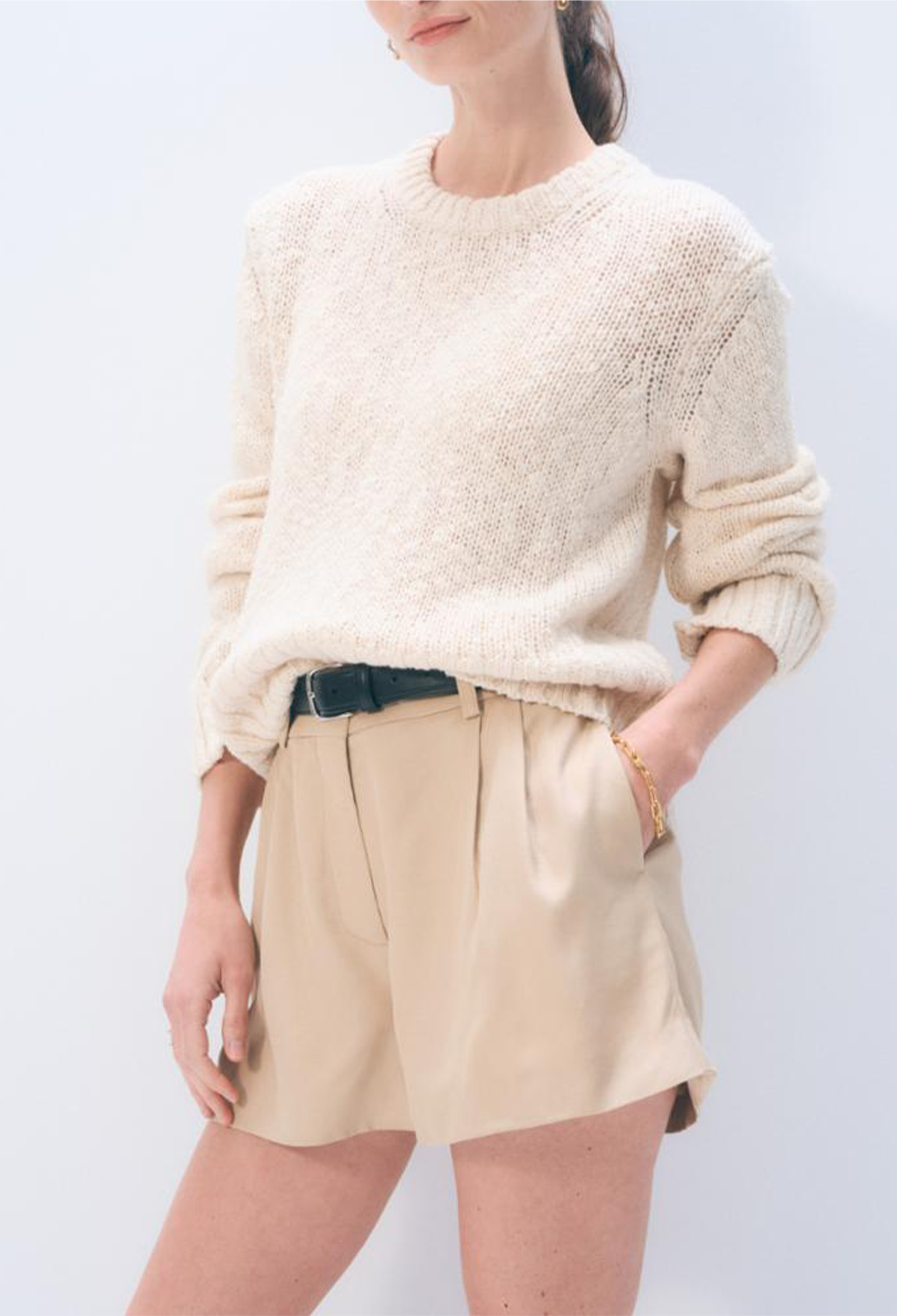 Person wearing a cream sweater and beige shorts on a light gray background