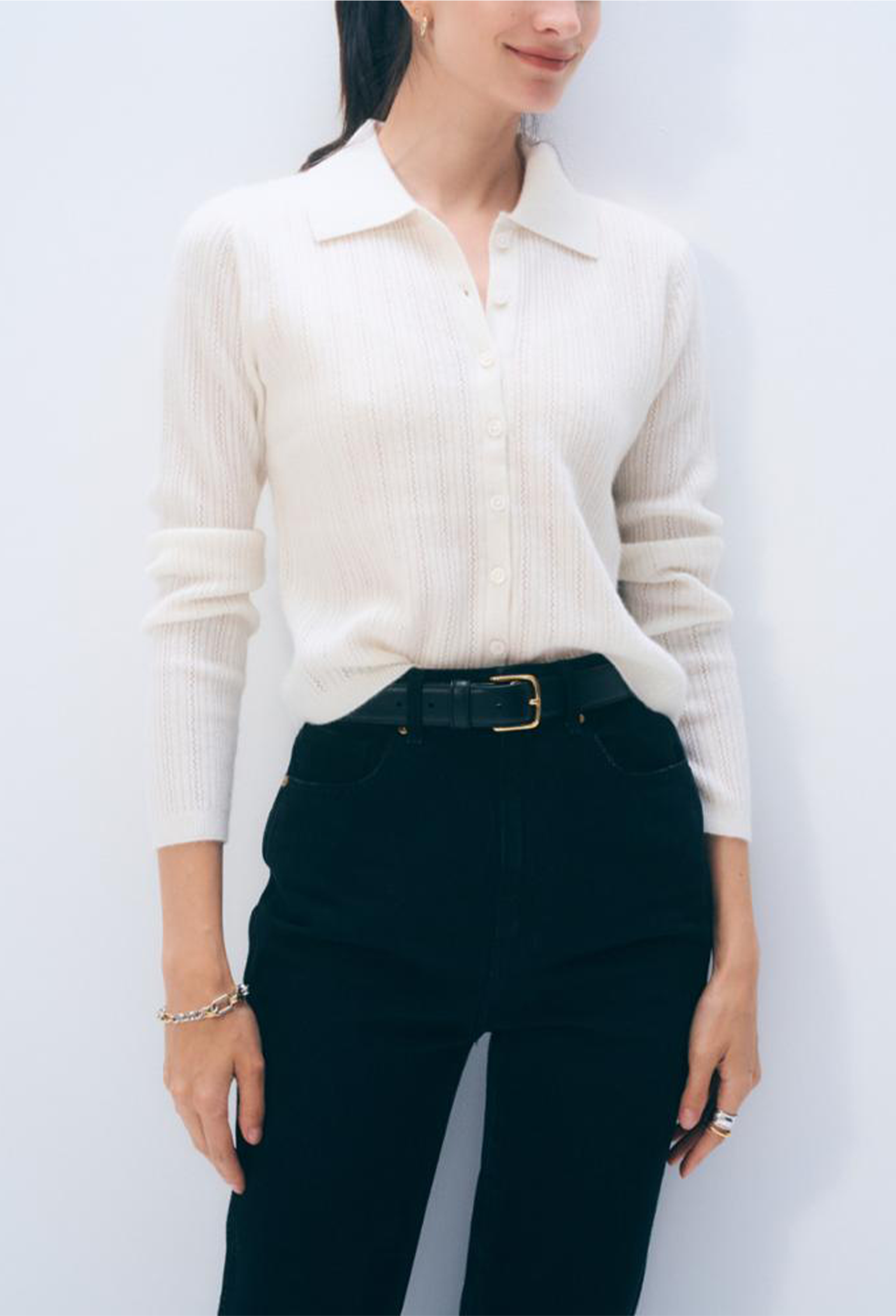 Person wearing a white ribbed sweater and black pants against a light background