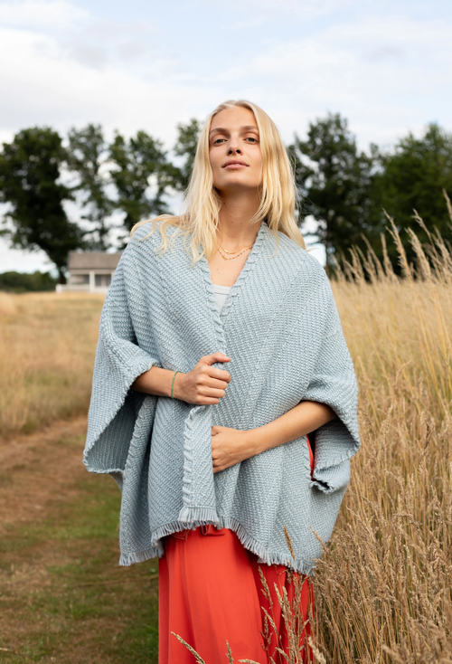 Woman wearing a light blue knitted shawl over a red dress in a field.