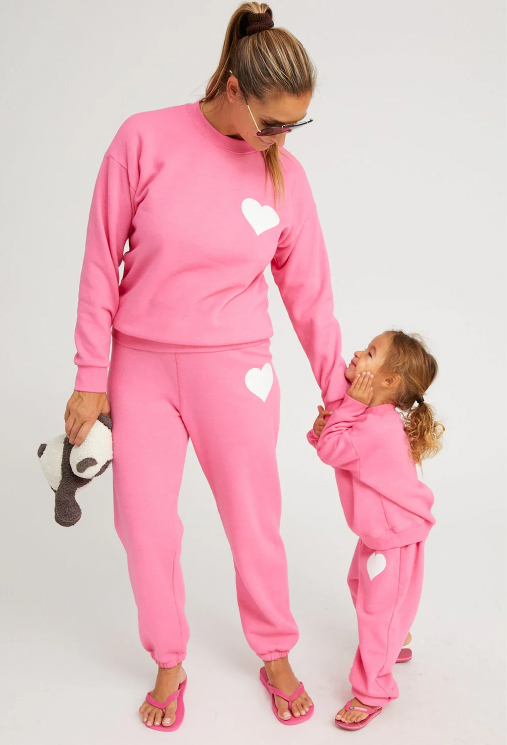 Woman and child wearing matching pink outfits with heart designs on a plain background