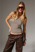 Woman wearing a striped tank top and brown pants against a gray background