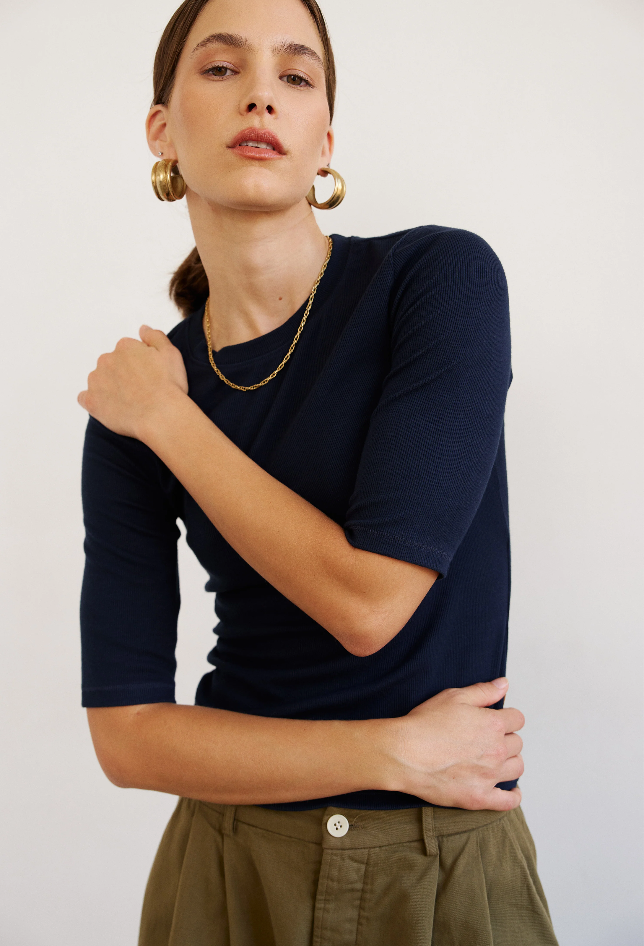Woman wearing a navy blue top and green pants against a white background