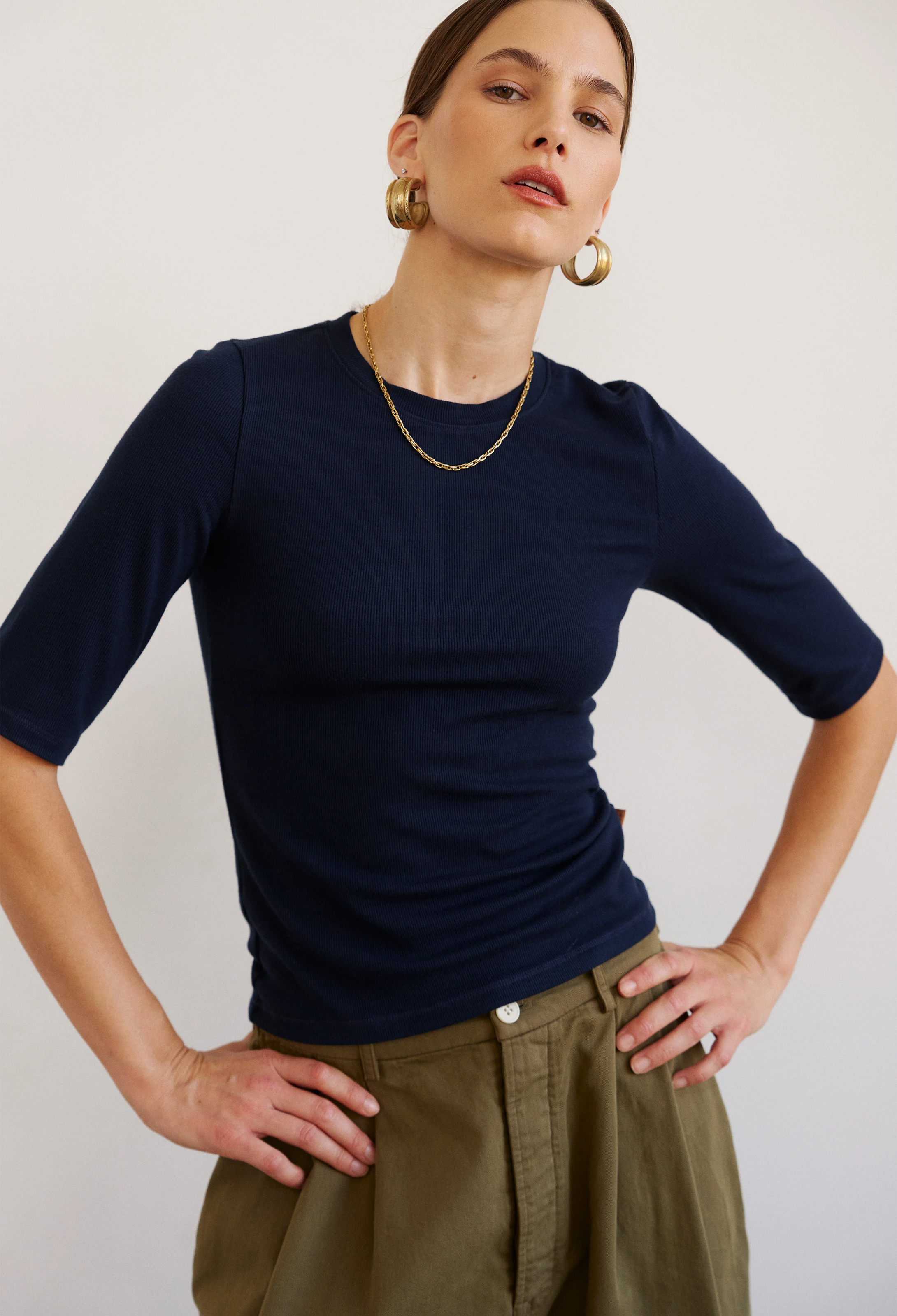 Woman wearing a navy blue top and green pants against a plain background