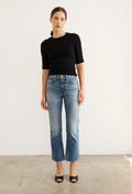 Woman wearing a black top and blue jeans against a white background