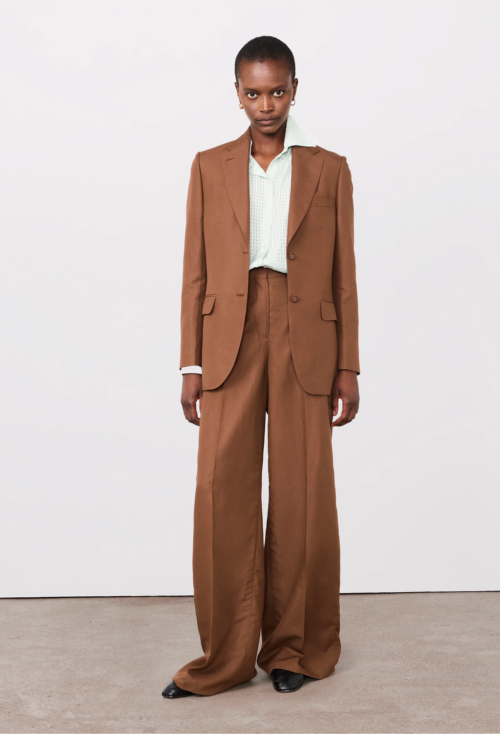 Person wearing a brown suit with a white shirt on a plain background