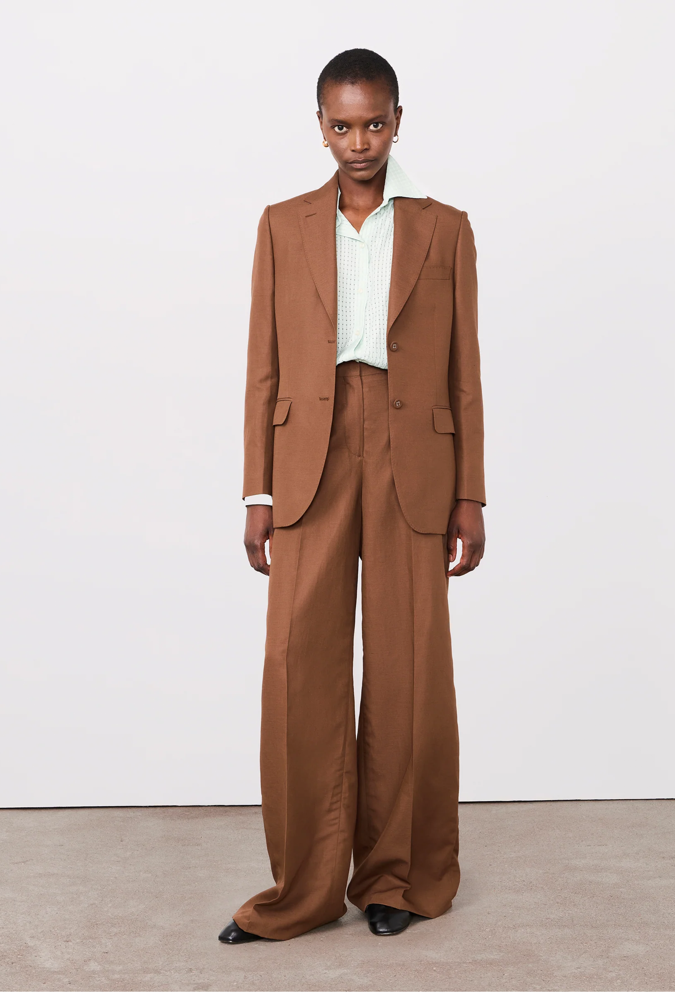 Person wearing a brown suit with a white shirt on a plain background