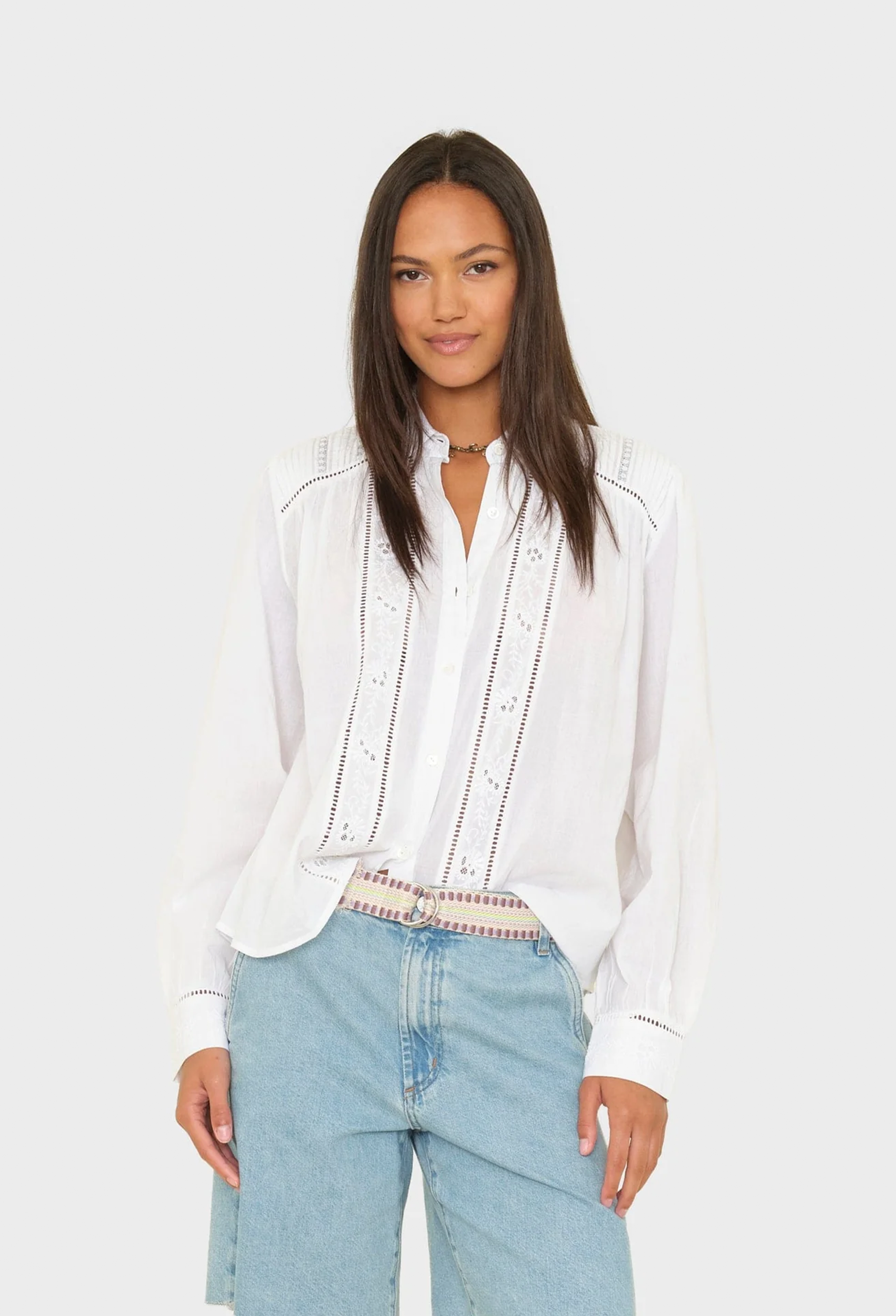 Woman wearing a white blouse with lace details and light blue jeans on a white background