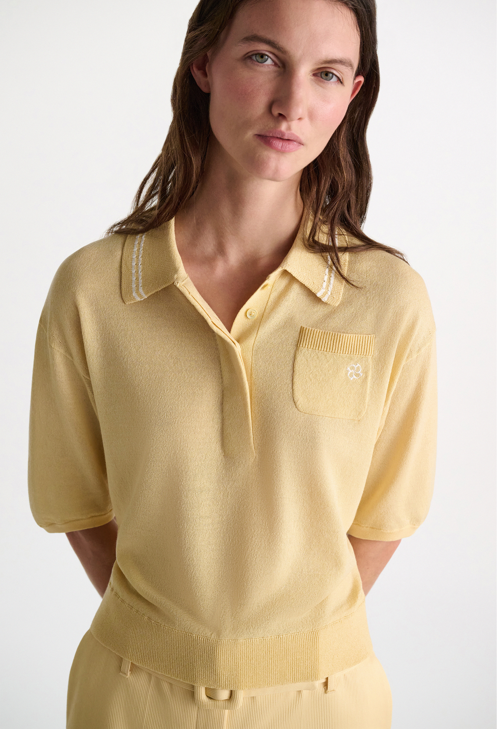 Woman wearing a yellow knit polo shirt on a white background