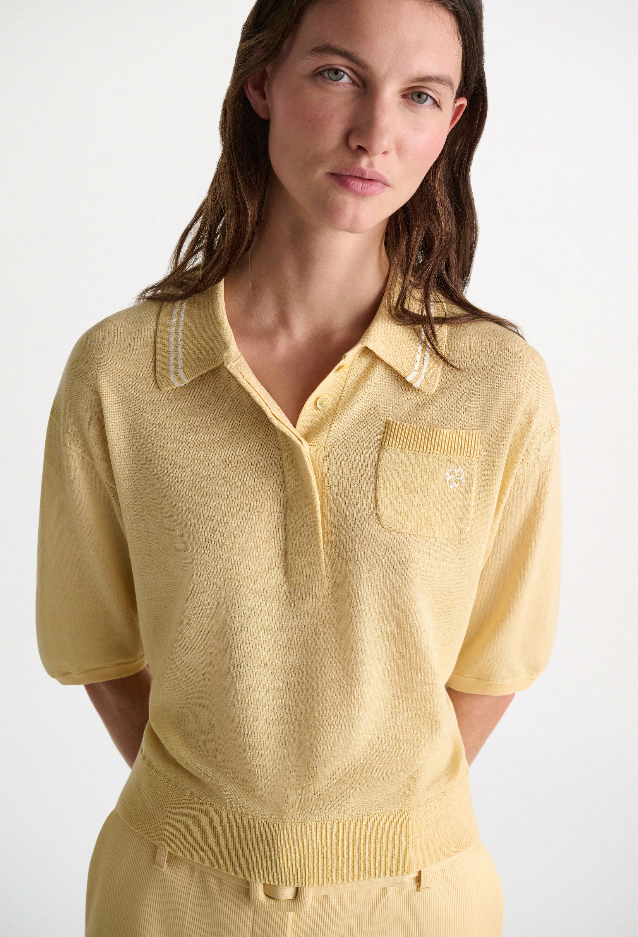 Woman wearing a yellow knit polo shirt on a white background