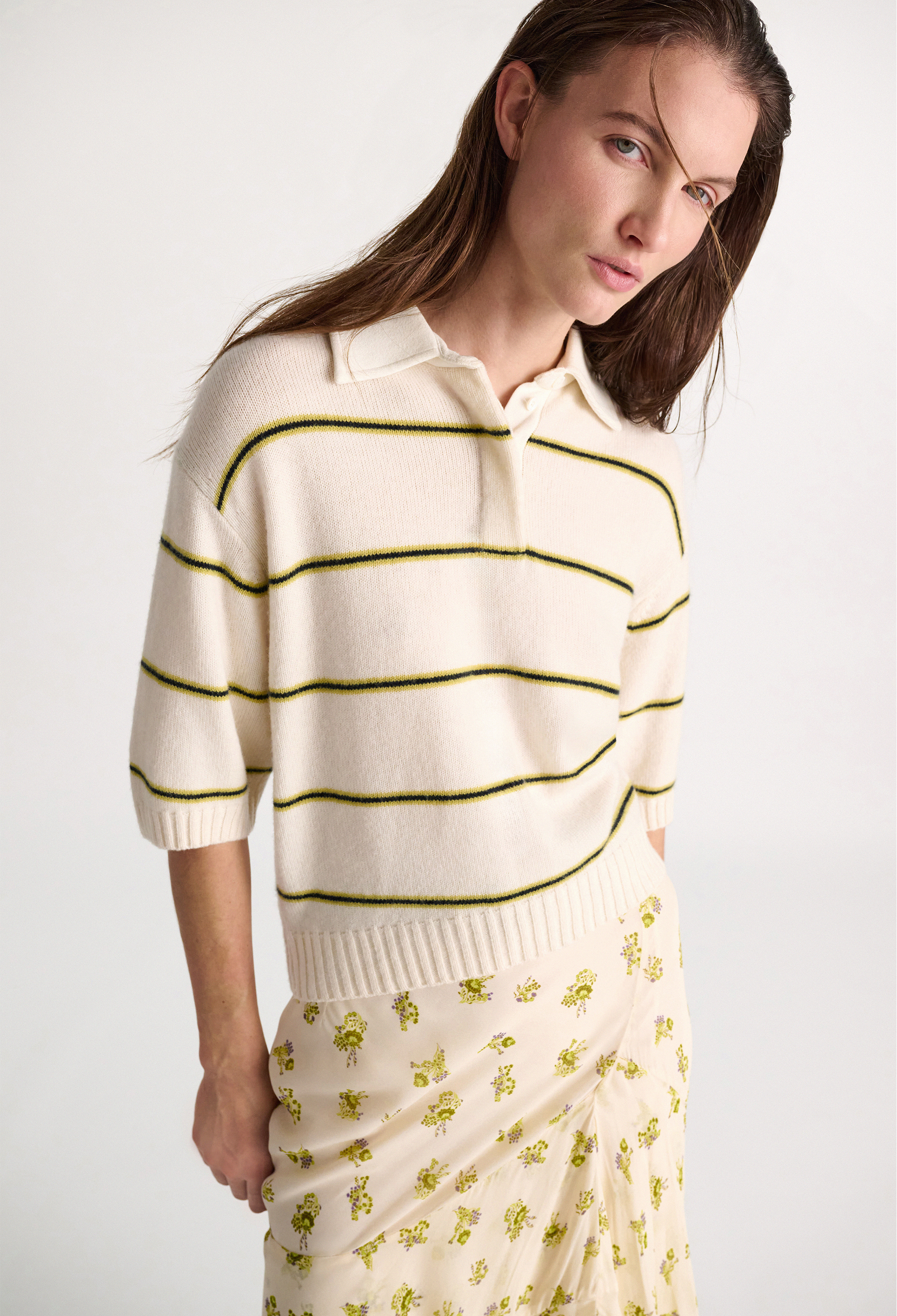 Woman wearing a cream sweater with green stripes and a floral skirt on a white background