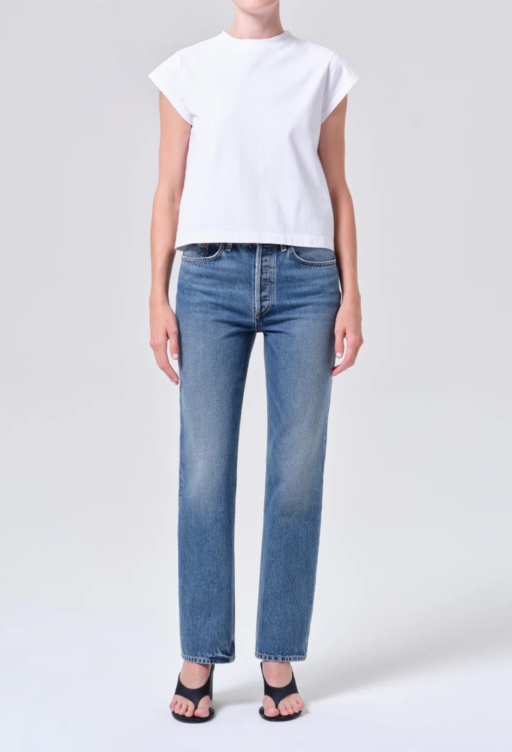 Person wearing a white t-shirt and blue jeans on a light gray background