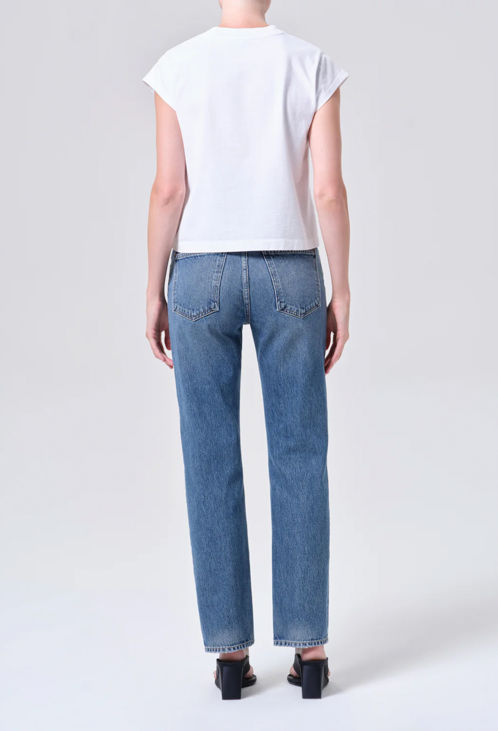 Person wearing blue jeans and a white top on a plain background