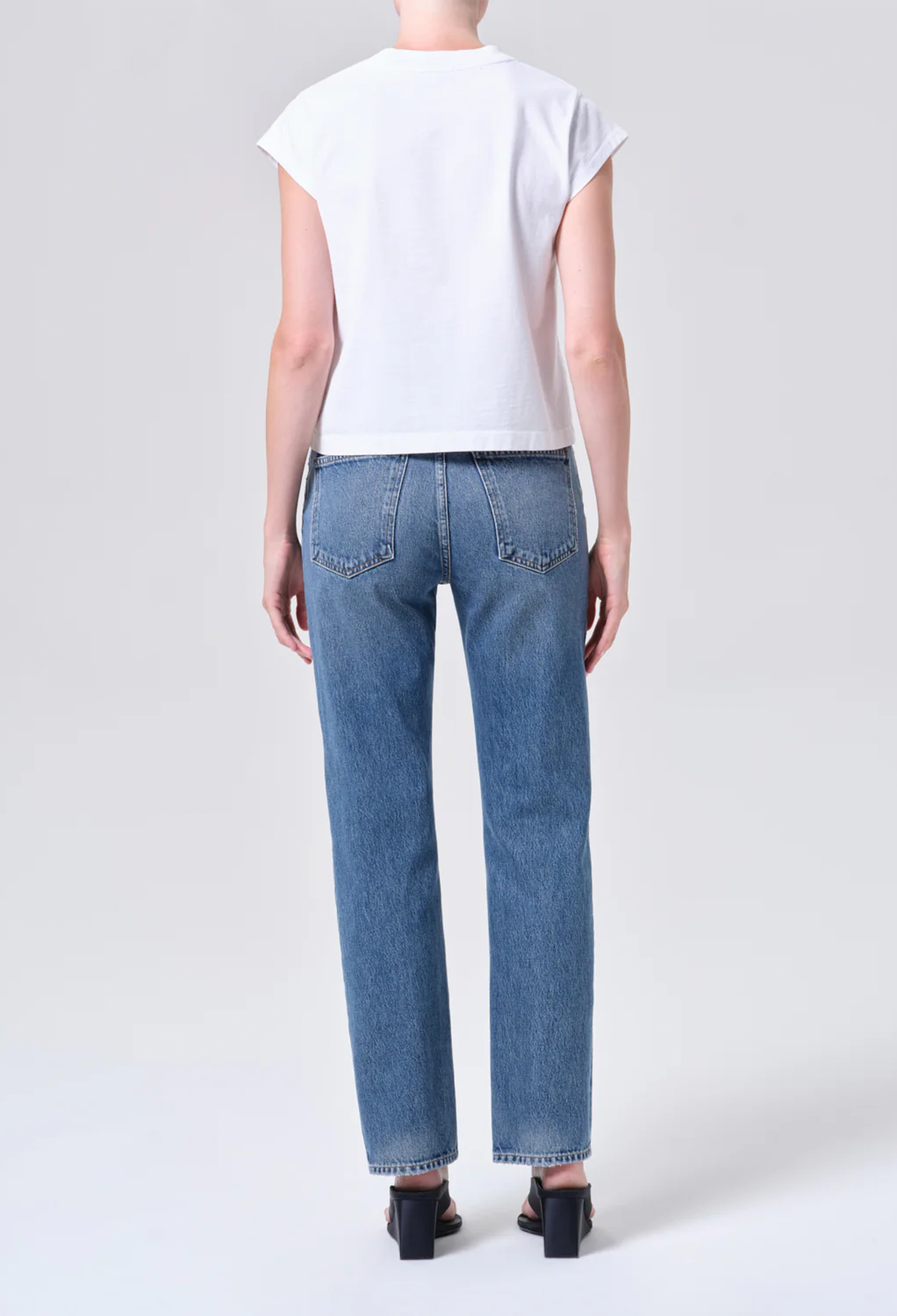 Person wearing blue jeans and a white top on a plain background
