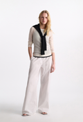 Woman wearing a beige sweater with a black collar and white pants on a white background