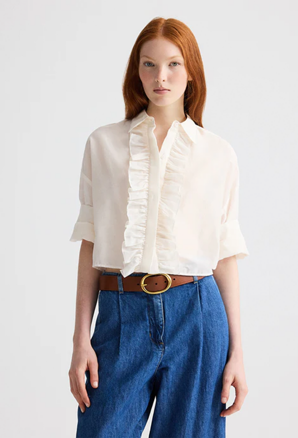 Woman wearing a white blouse with ruffles and blue jeans on a plain background
