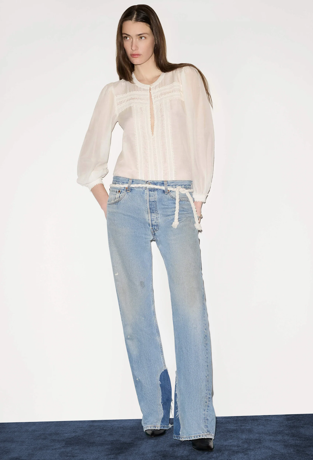 Woman wearing a white blouse and light blue jeans on a plain background