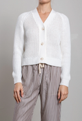 Person wearing a white textured cardigan and striped pants on a gray background