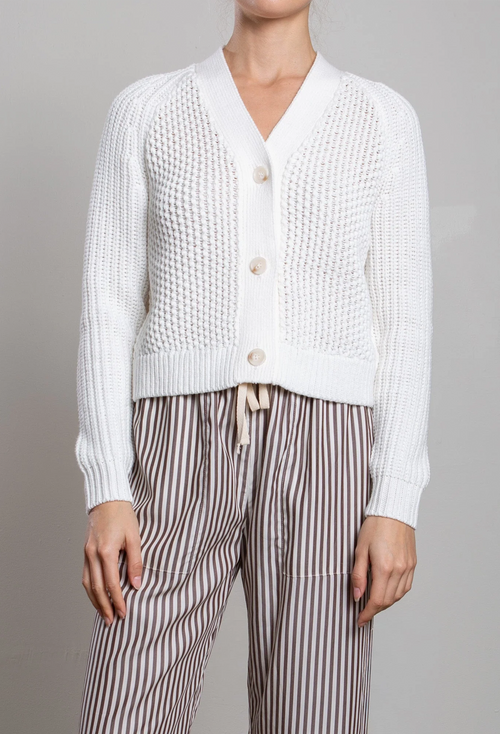 Person wearing a white textured cardigan and striped pants on a gray background