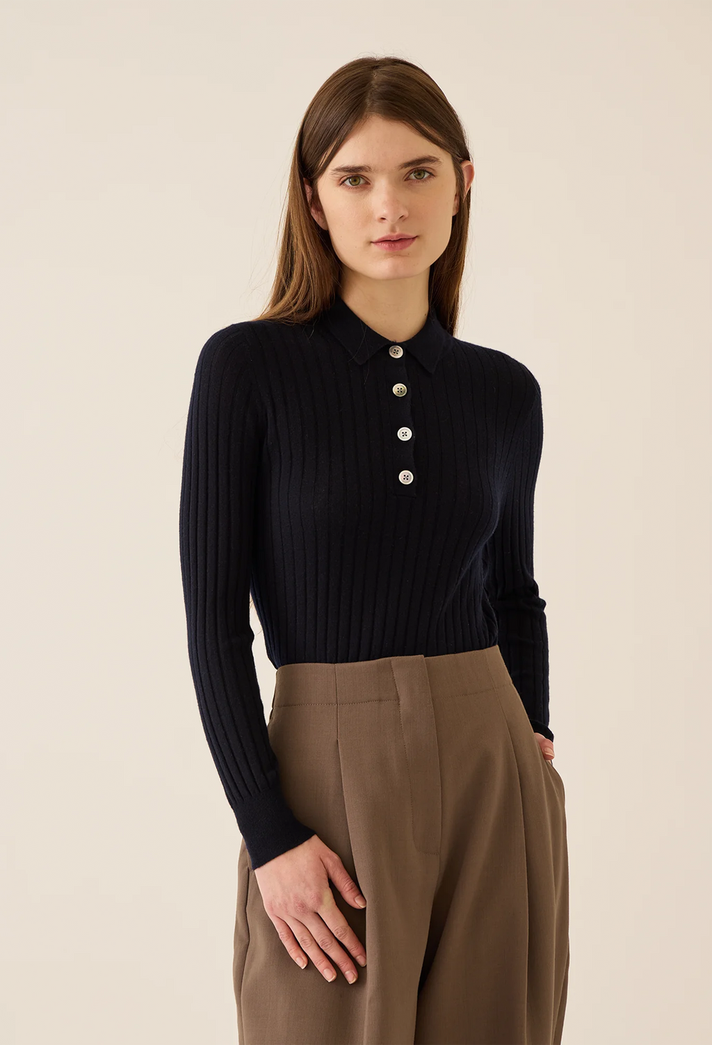 Woman wearing a navy ribbed sweater with buttons and brown pants on a beige background