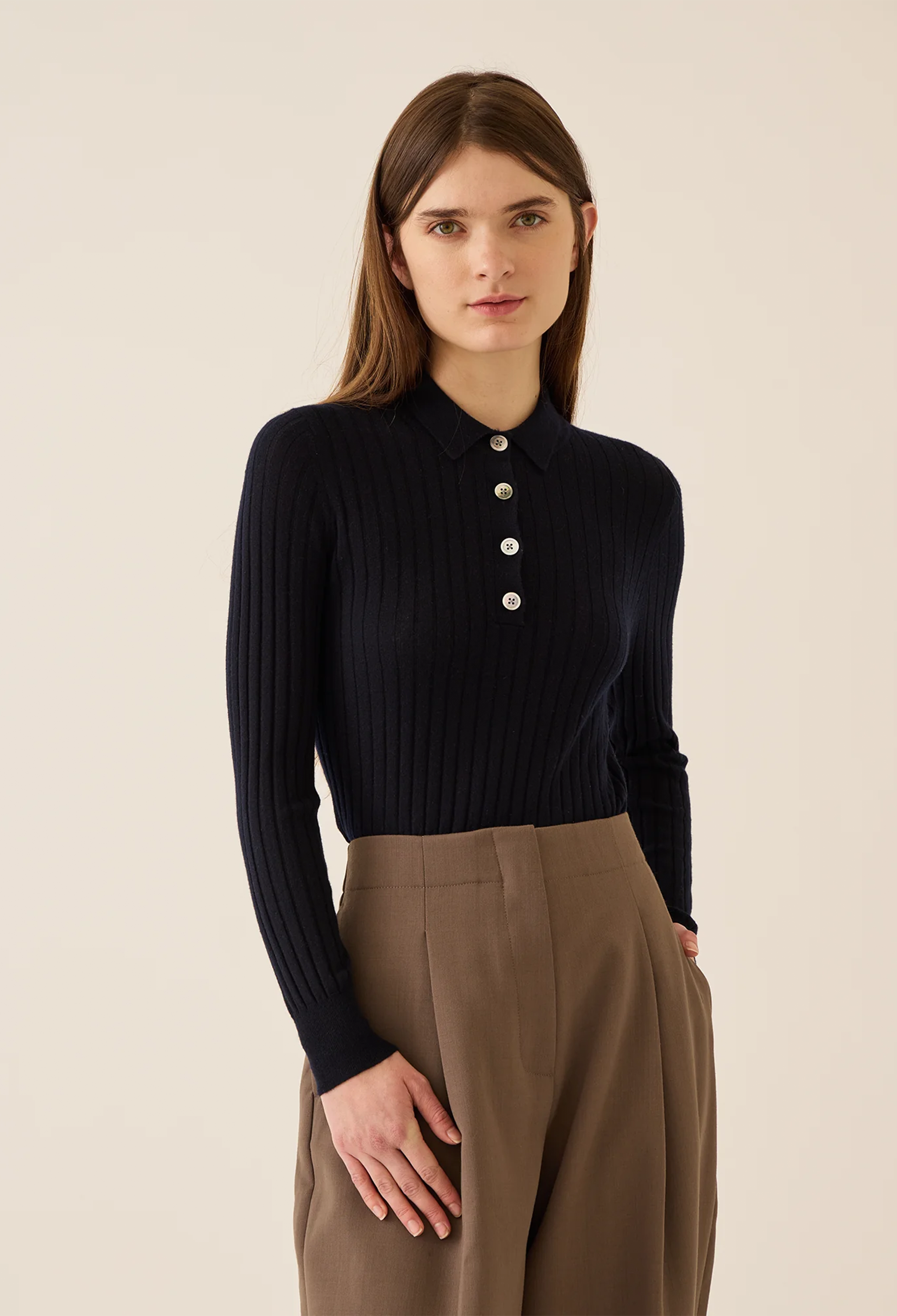 Woman wearing a navy ribbed sweater with buttons and brown pants on a beige background