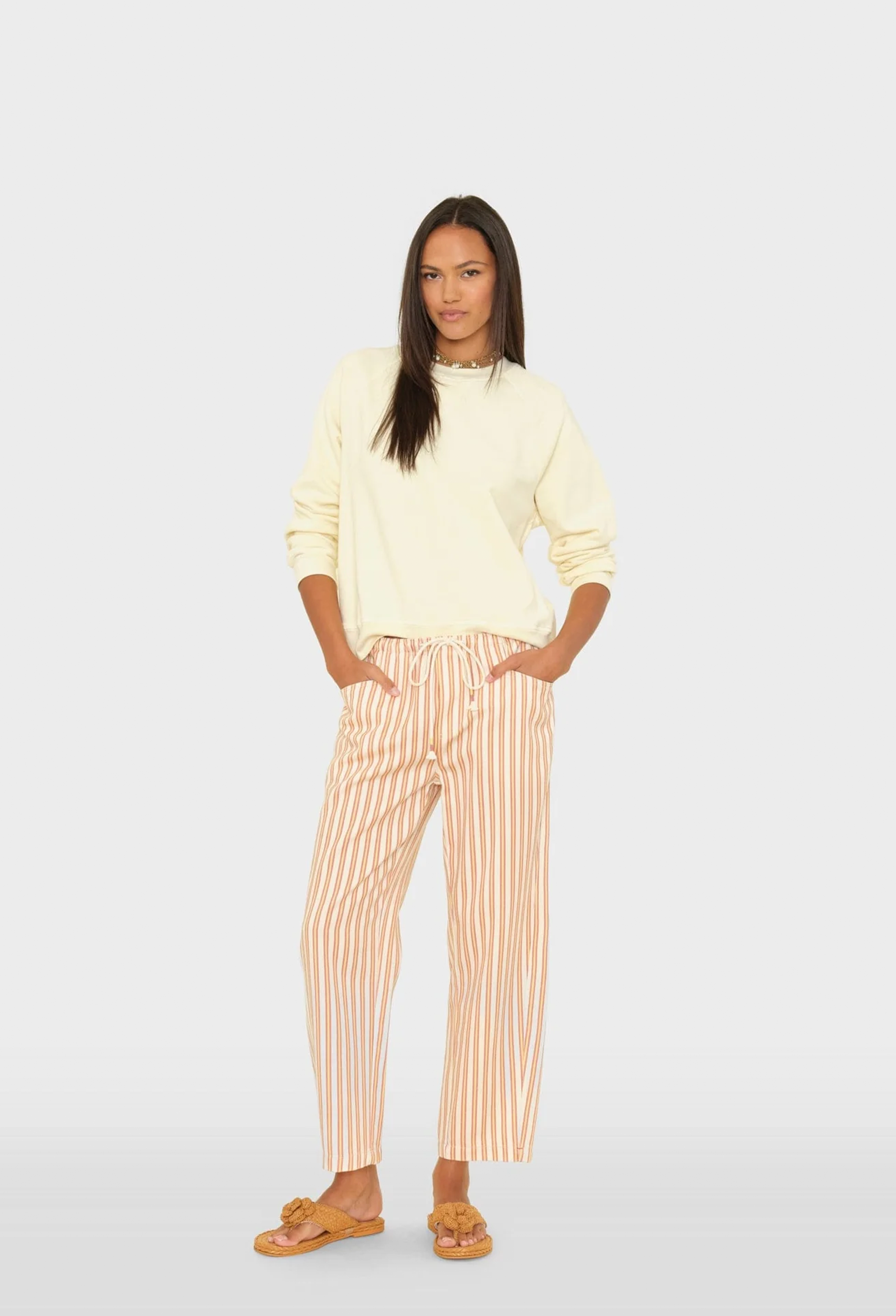 Woman wearing a light yellow sweater and striped pants on a white background