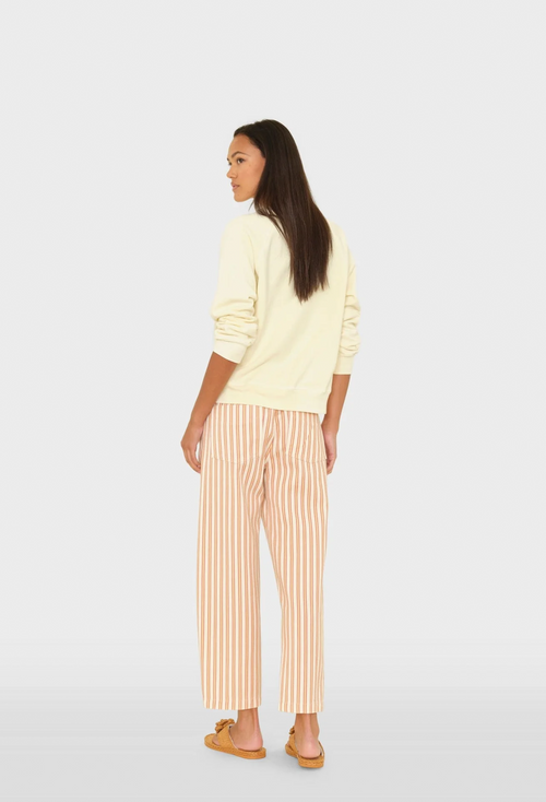 Woman wearing a light yellow sweater and striped pants on a white background
