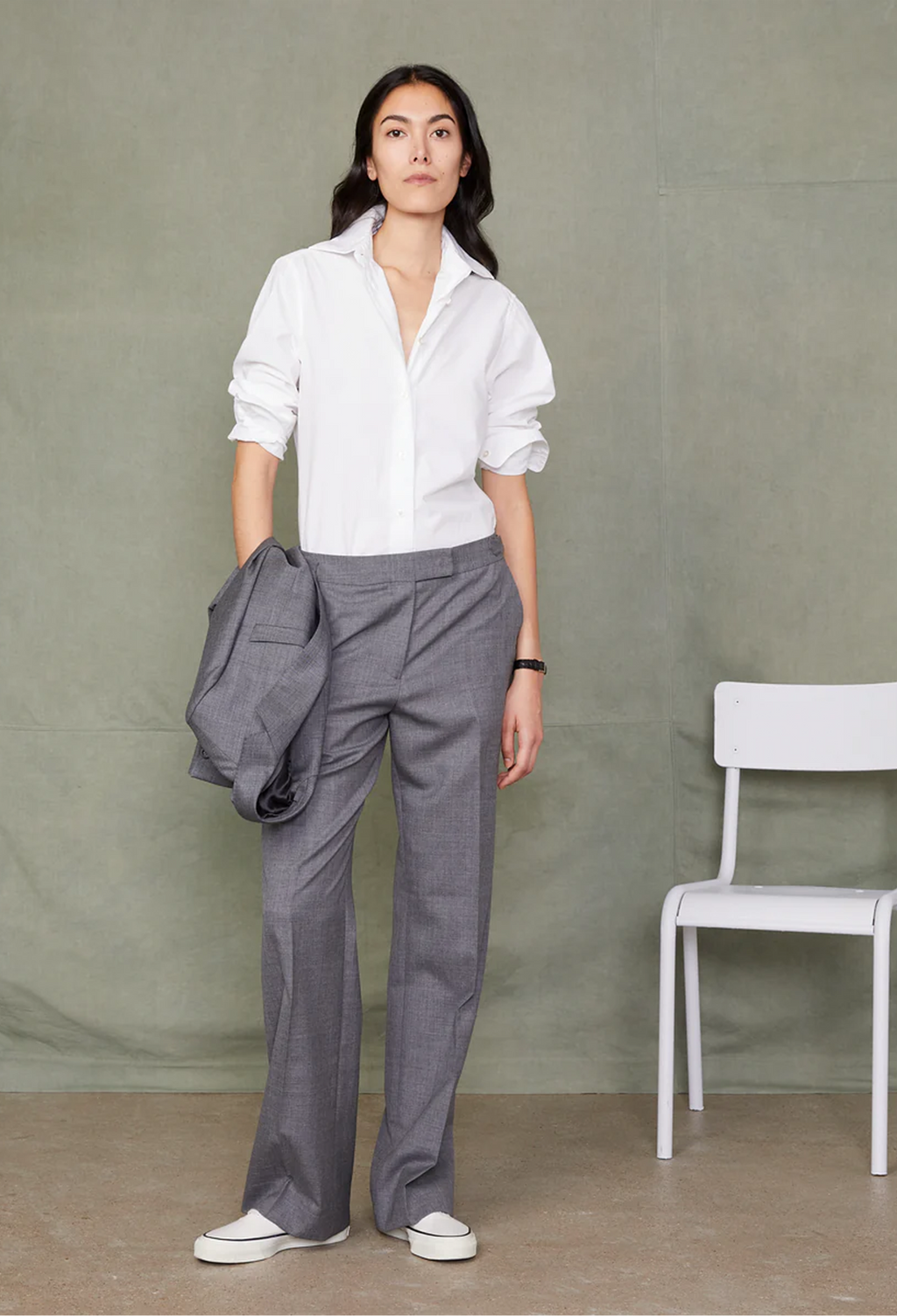 Woman wearing a white shirt and gray pants standing against a plain background