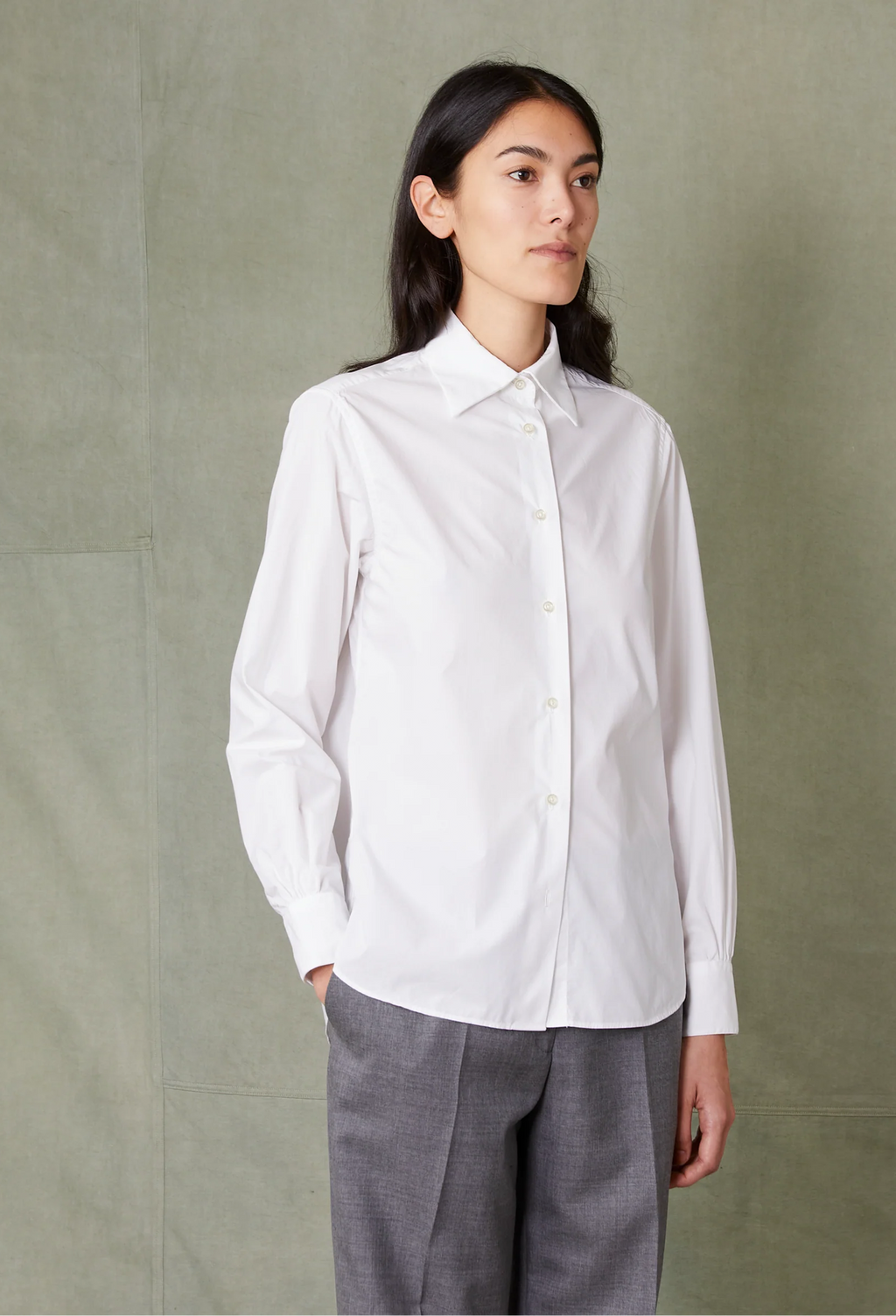 Person wearing a white shirt and gray pants against a plain background