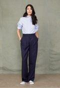 Woman wearing a light blue shirt and dark blue pants against a plain background