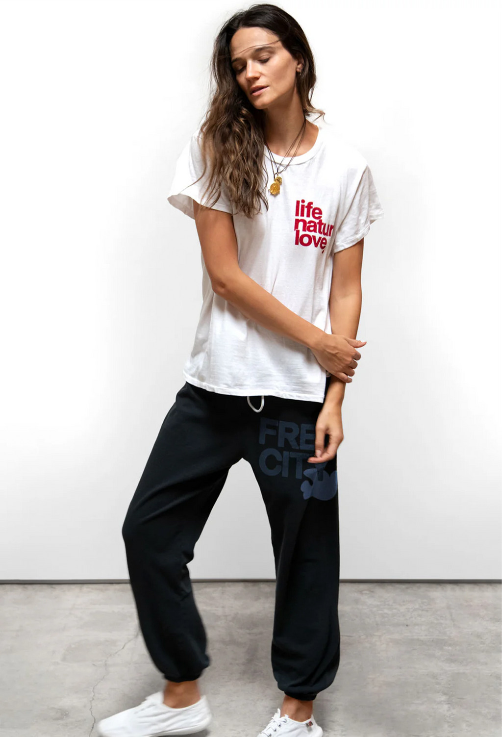 Woman wearing a white t-shirt with text and blue pants with 'Freecity' logo on a plain background