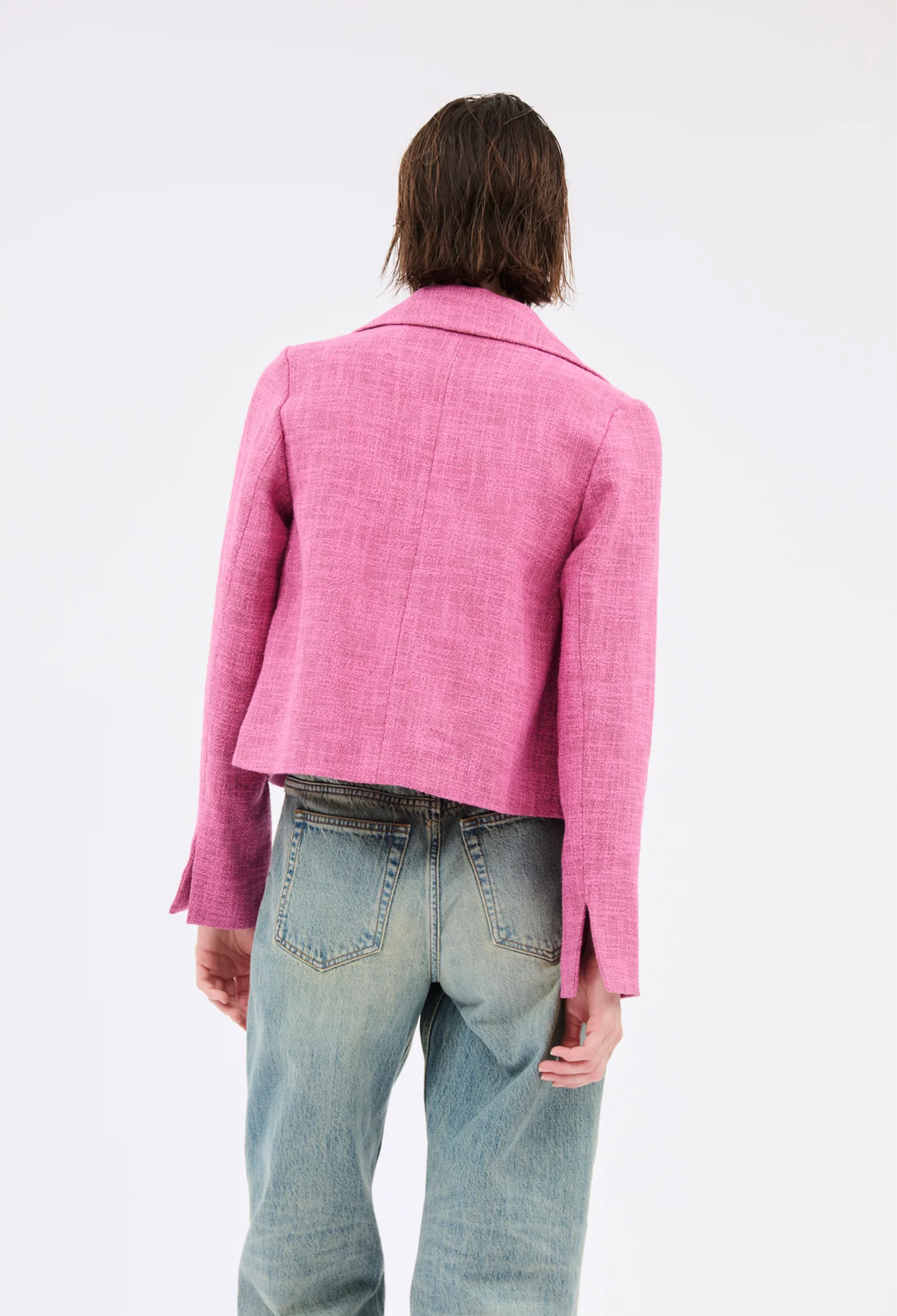 Person wearing a pink blazer and blue jeans on a white background