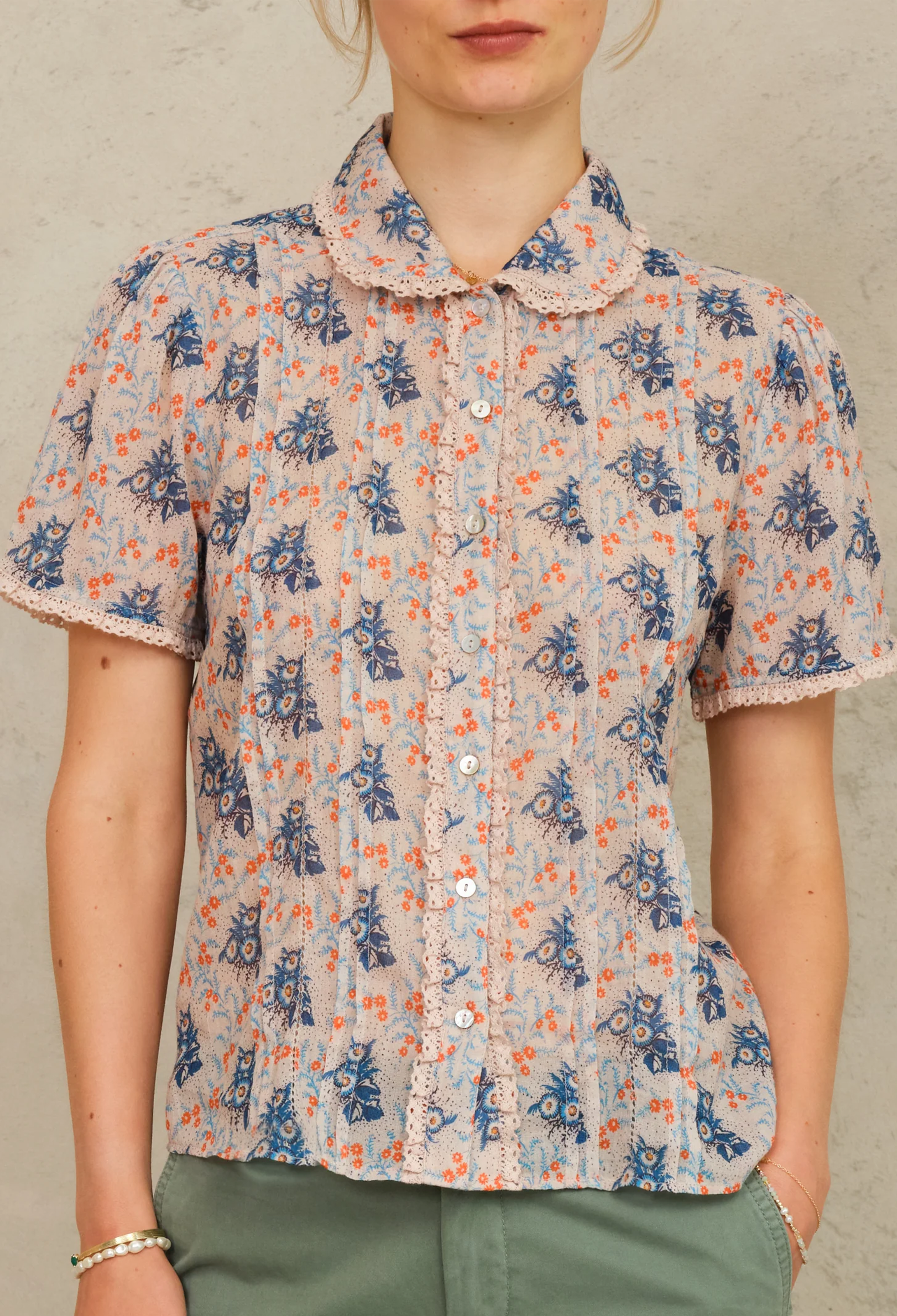 Person wearing a short-sleeve blouse with a floral pattern on a neutral background