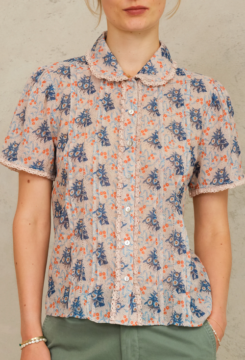 Person wearing a short-sleeve blouse with a floral pattern on a neutral background