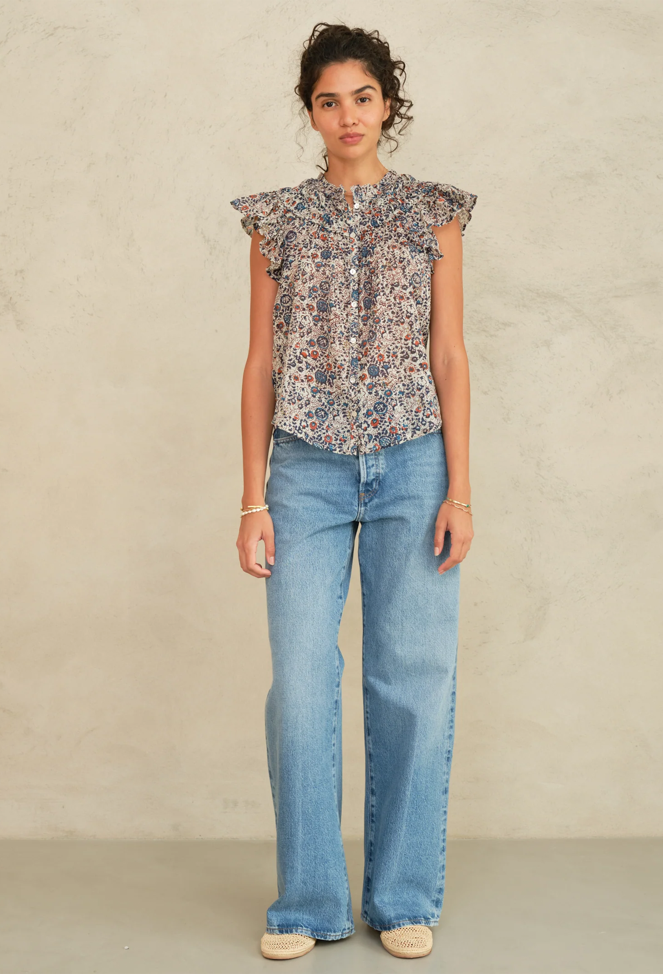 a model wearing a frilly short sleeve top with a floral print on a grey background