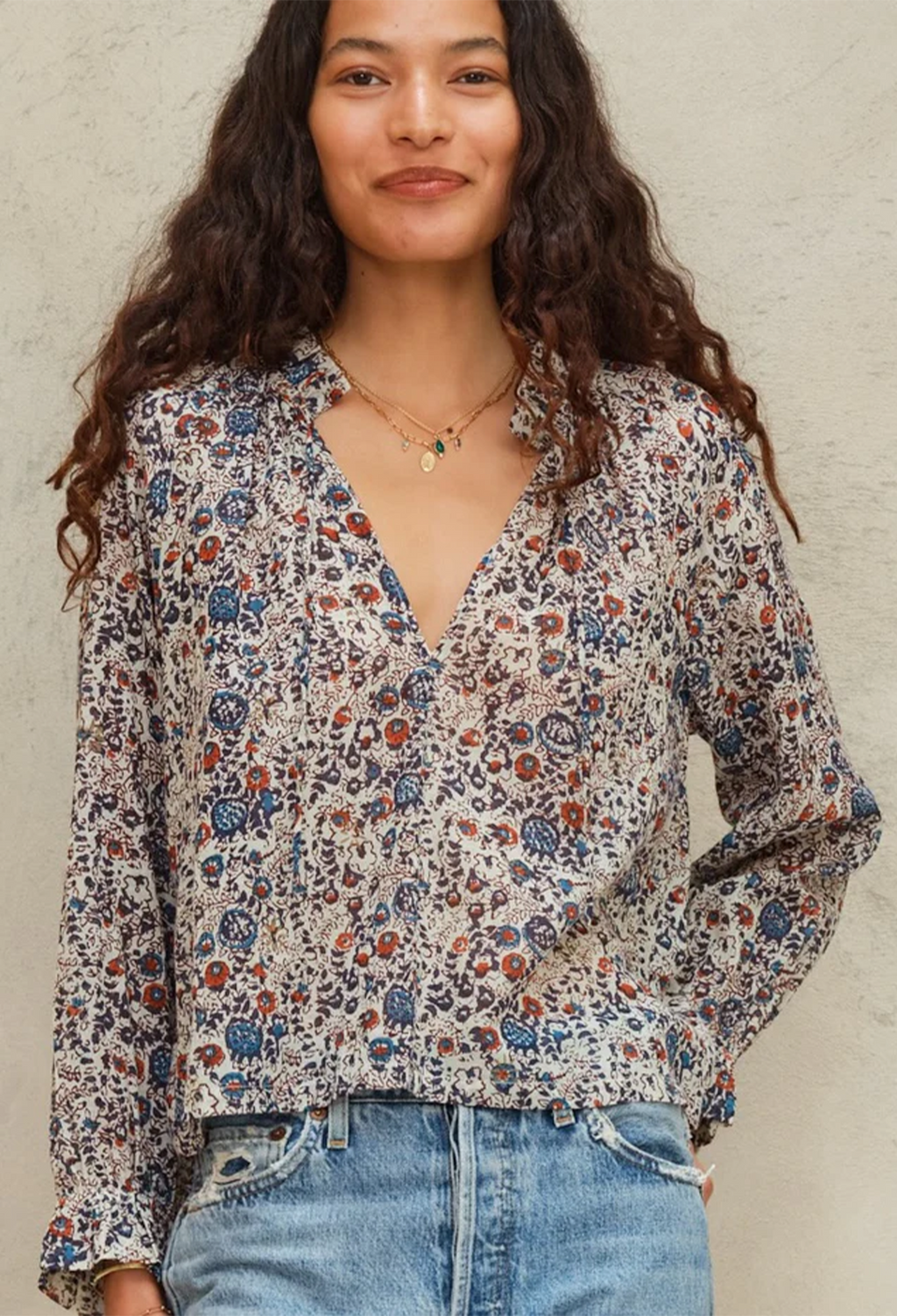 Woman wearing a floral blouse and jeans against a neutral background