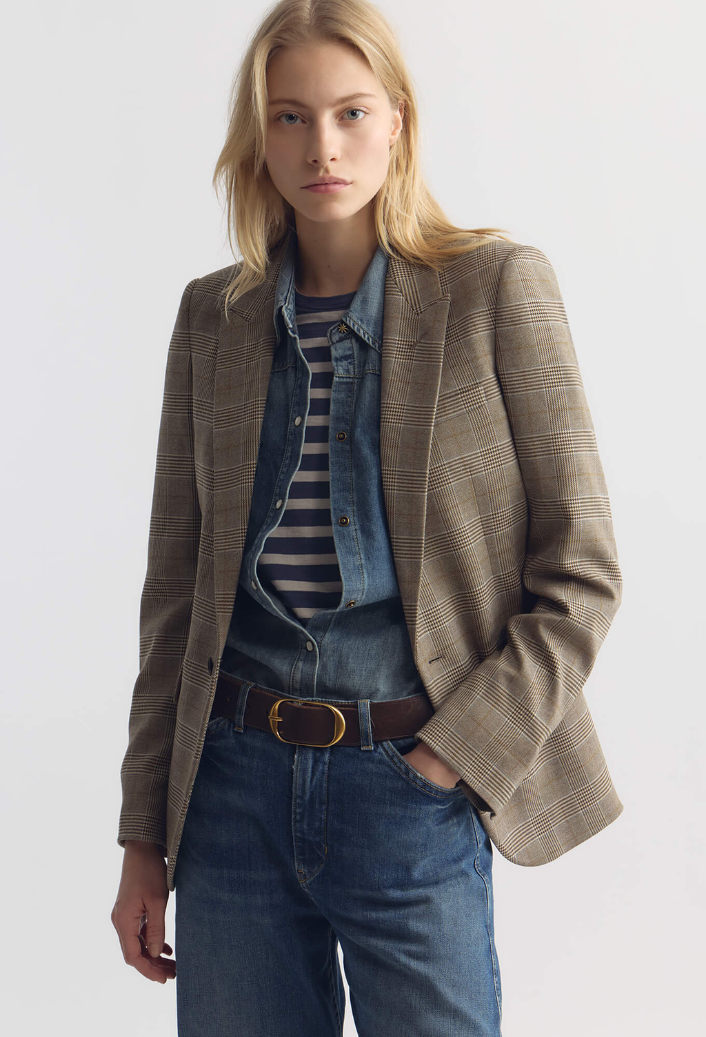 Woman wearing a brown blazer over a striped shirt and jeans on a white background