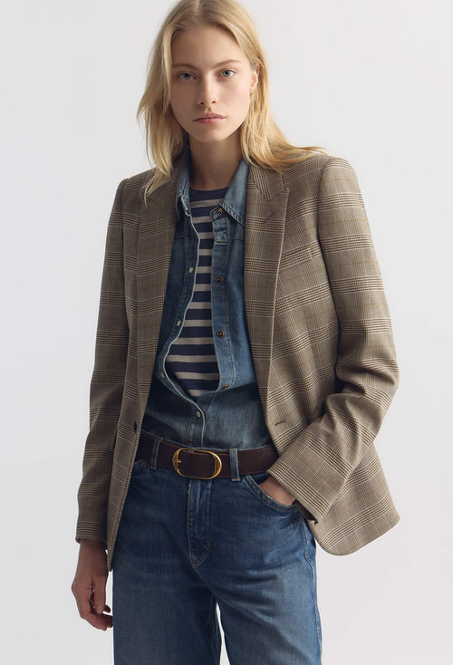 Woman wearing a brown blazer over a striped shirt and jeans on a white background