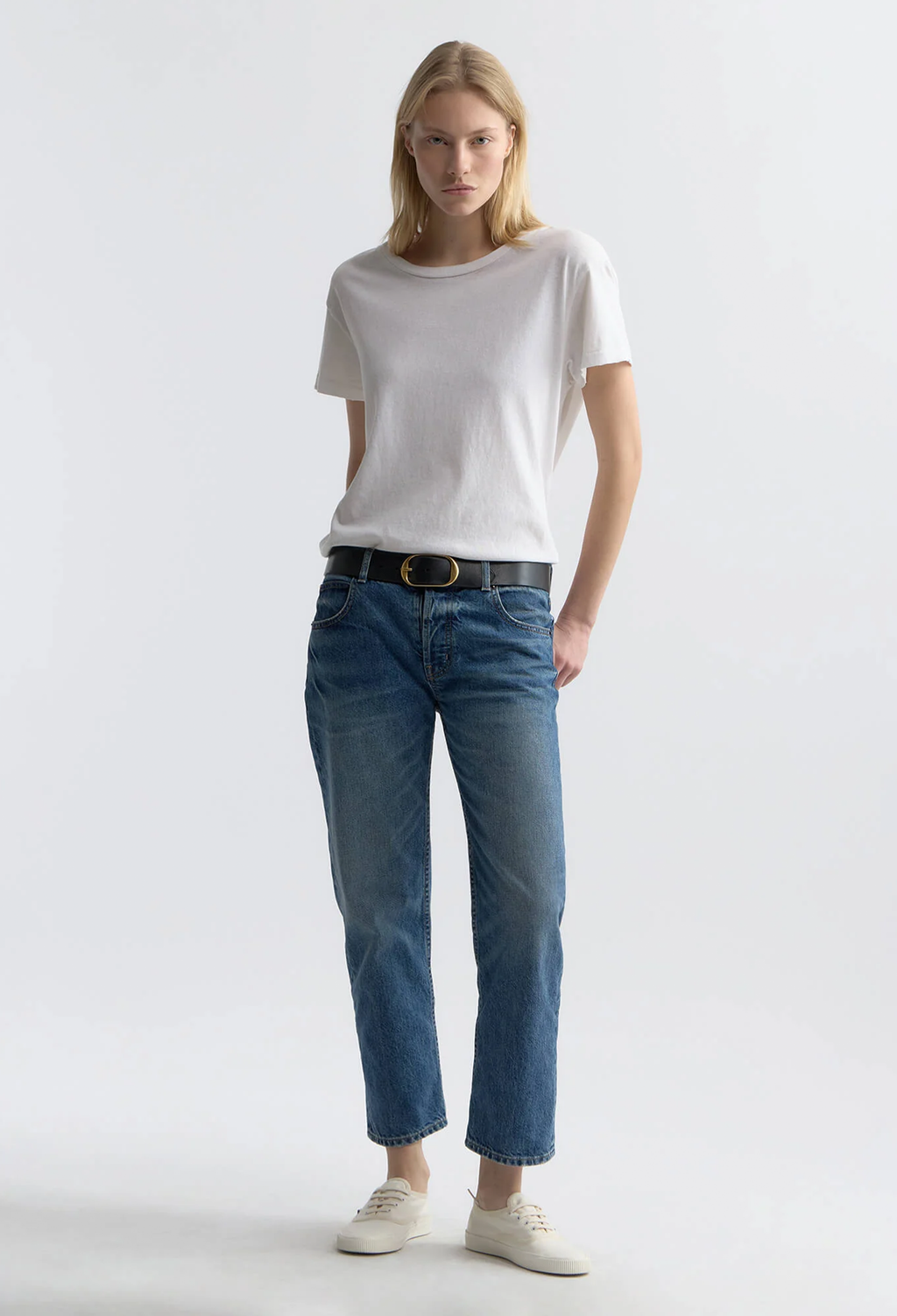 Woman wearing a white t-shirt and blue jeans on a plain background