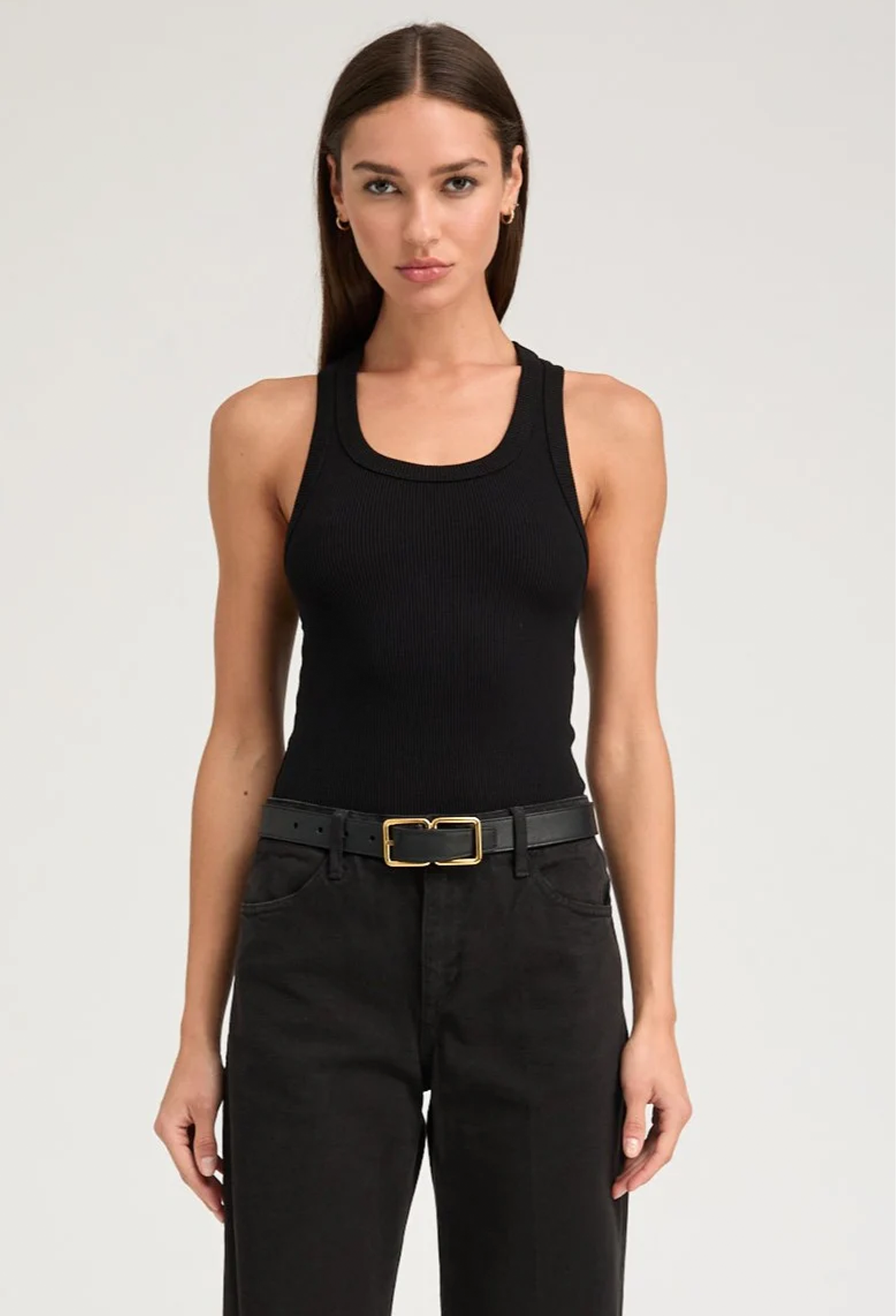Woman wearing a black tank top and black pants with a gold belt on a white background