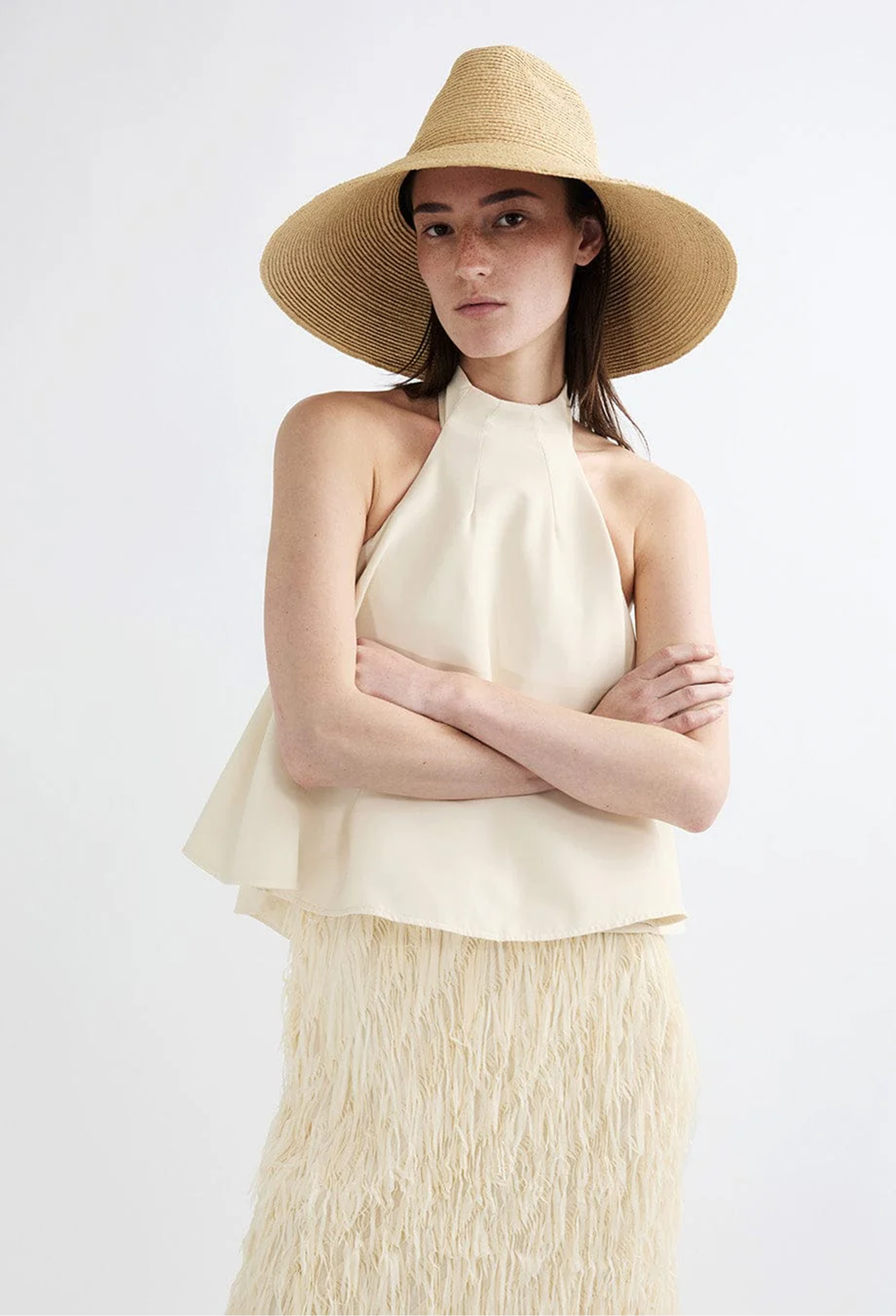 Woman wearing a beige sleeveless top and skirt with a wide-brimmed hat on a white background
