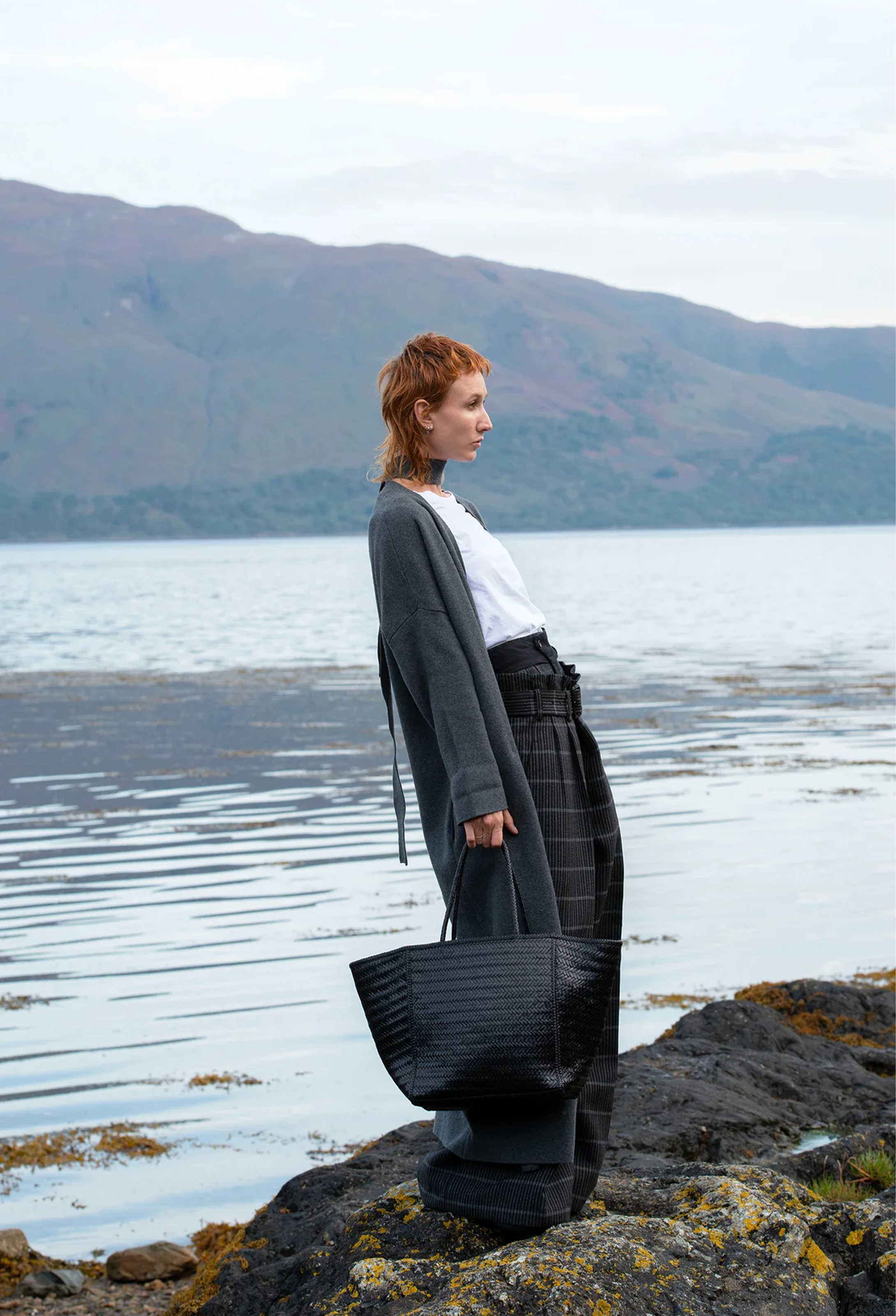 a woman holding a large black leather bag by a body of water